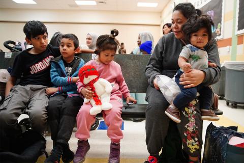 Marcela Funes, 3, wears an earpiece allowing her to listen to an interpreter during a presentation at Akron’s Findley Community Learning Center on Tuesday, Dec. 12, 2023. To the right, Marcela's mother, Sheila Soto, holds her infant nephew Ian Hernandez. Sitting to the left are Sheila's son Yago Soto, 5, and the son a of family friend, Erick Hernandez, 10.
